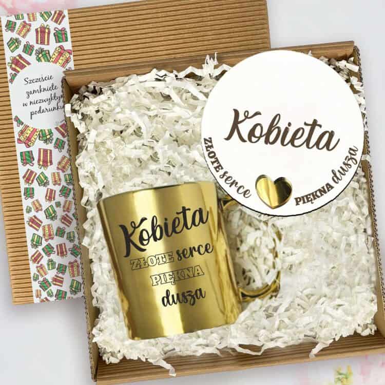 Zbliżenie na zestaw w pudełku: złoty kubek oraz etykieta „Kobieta”