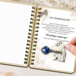 Otwarty album na pieniądze ze złotą spiralą, pokazujący kartkę z nadrukiem życzeń 'Na dojrzałość' oraz ilustracją klucza i banknotu